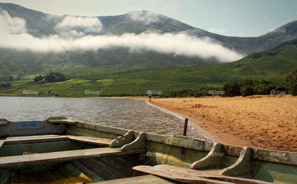 Beautiful lakeside scenery with sandy beach, old wooden boat and mountains in the background at Loch na fooey, Connemara, Ireland