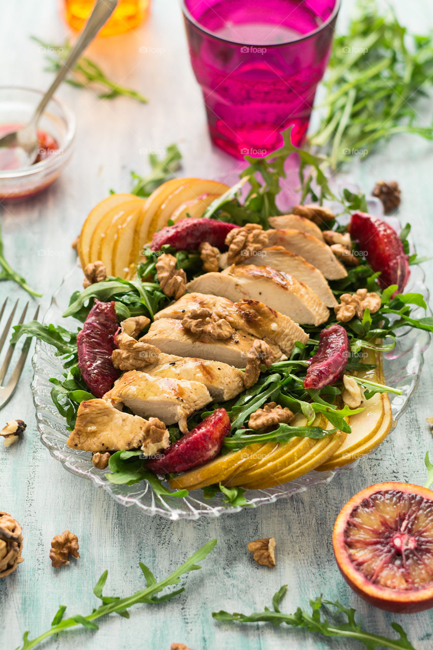 Salad with chiken bearst, pear, red orange fruit, walnuts and arugula leaves