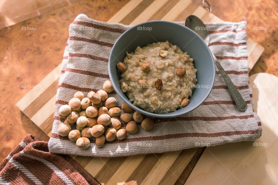 Cooked oatmeal in a deep gray plate with hazelnuts and honey.