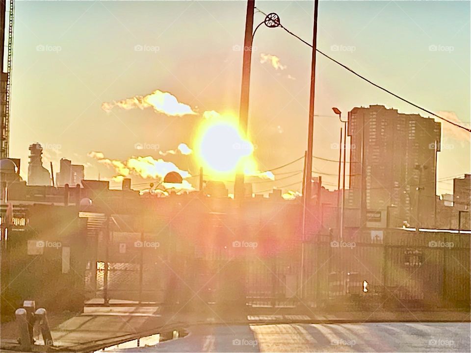 A fiercely bright glowing fireball is the sun that provides us all with warmth and energy. It is on its way to setting behind the horizon at Newtown Creek in Long Island City, Queens, NY. 2021. Hypnotic Productions