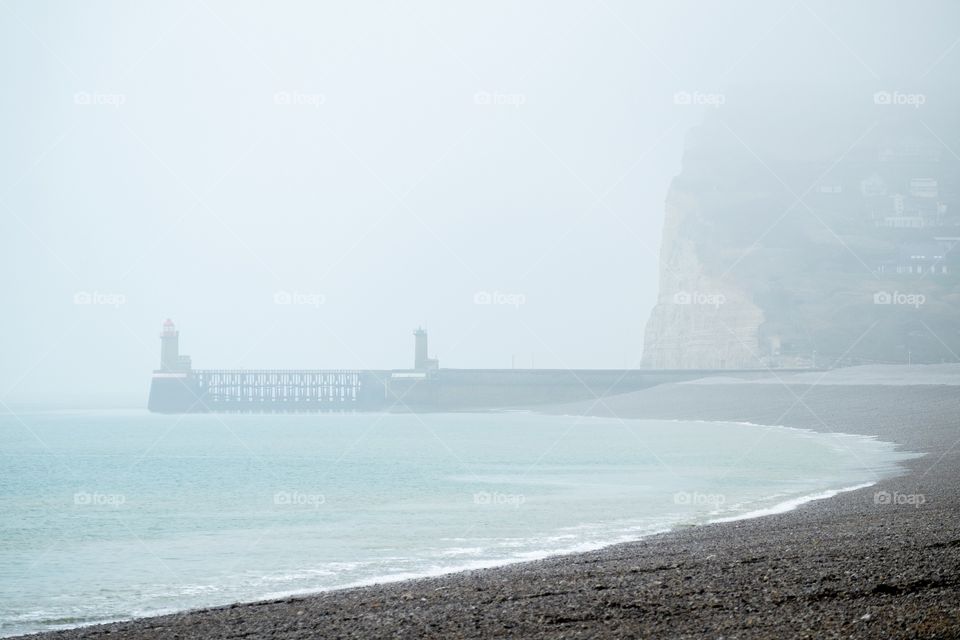 Misty landscape of the lighthouse, pier, cliffs and Pebble beach of Fécamp, Normandy, France