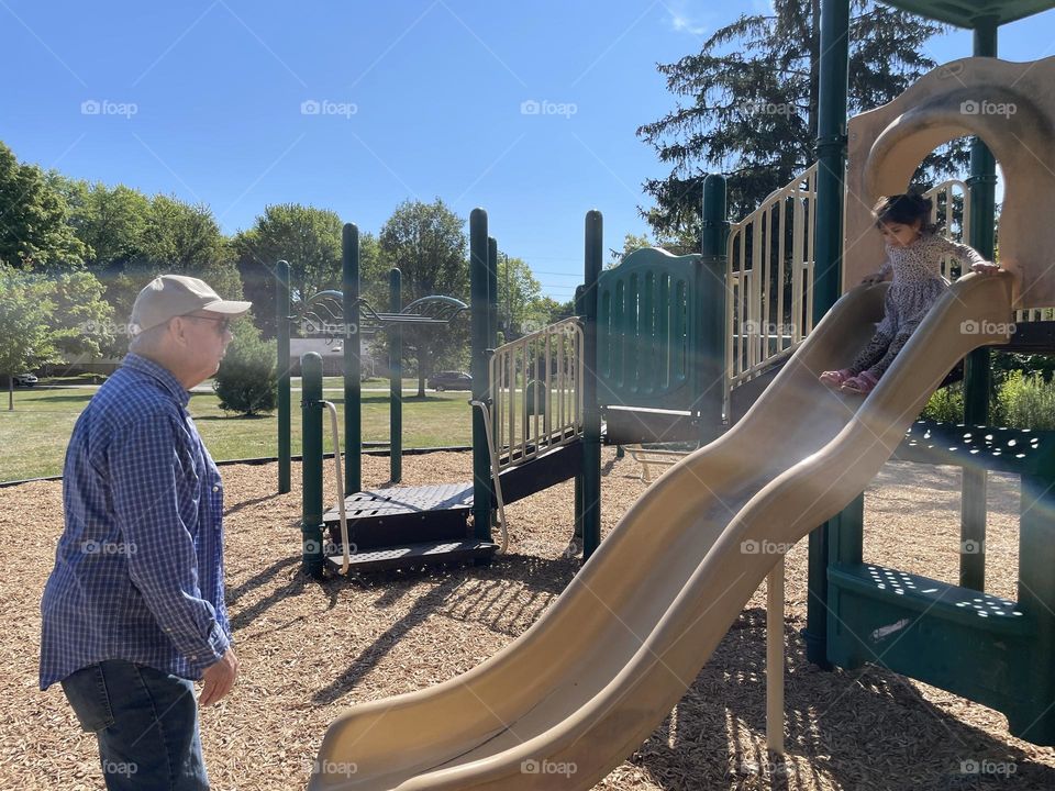 Grandfather waits for granddaughter to come down the slide, grandpa at the park with grandkid, having fun at the park with grandpa, sliding down the slide at the park