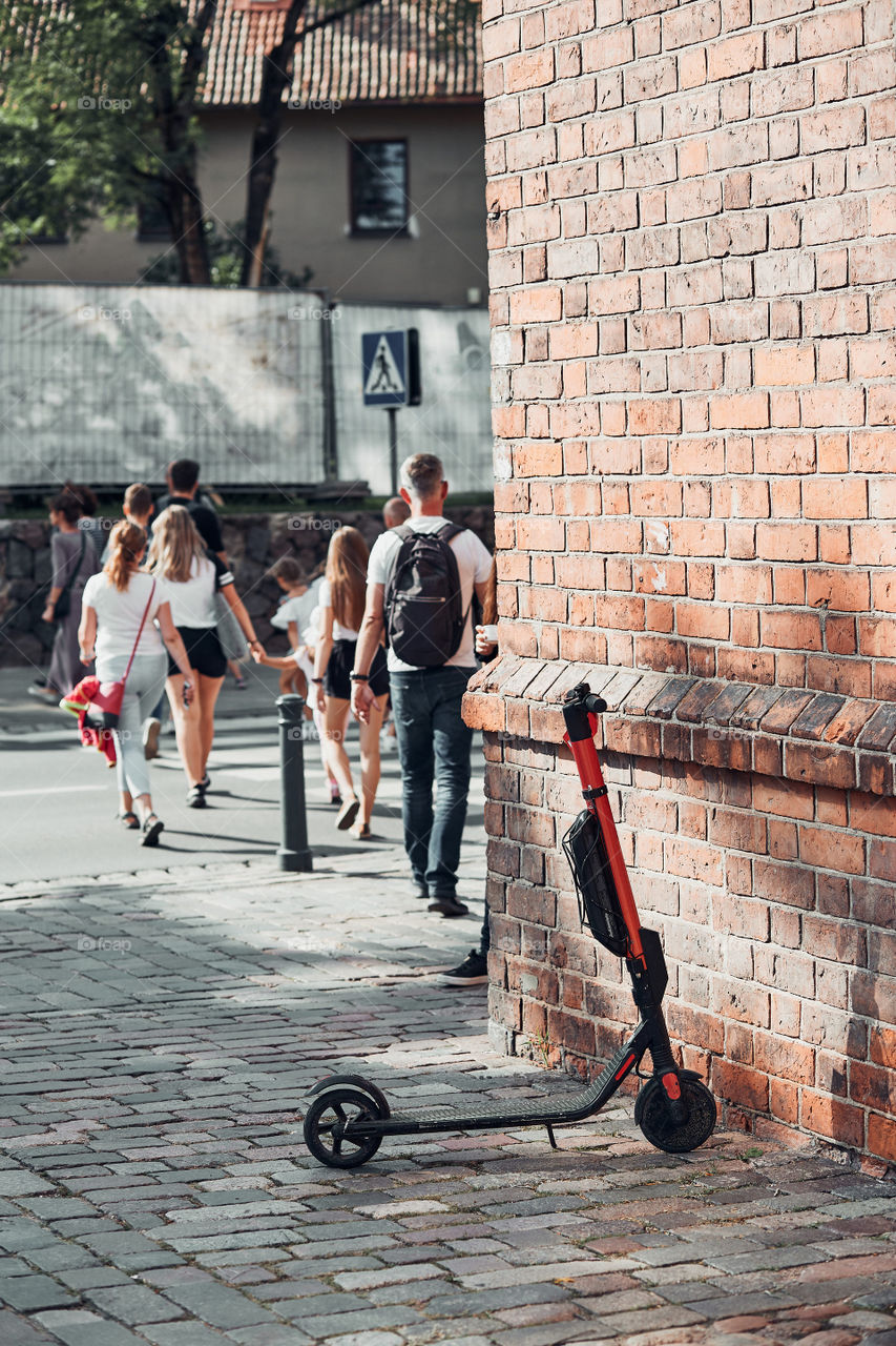 Electric scooter, e-scooter left in a center of town. Person arrived to work using electric scooter. Using rent service on smartphone. Candid people, real moments, authentic situations