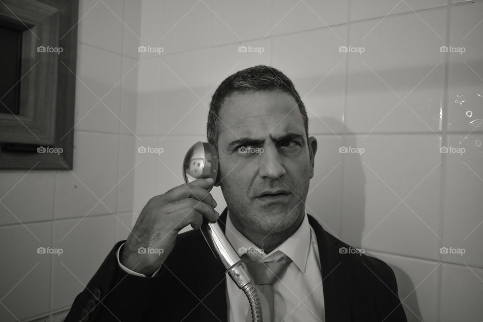 Man in suit staying in bathroom and listening shower head like talking on the phone. Simulation phone conversation with a shower head 