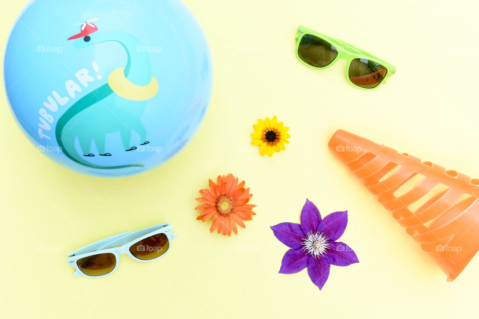 Flat lay of colorful summer objects including sunglasses, flowers and a ball