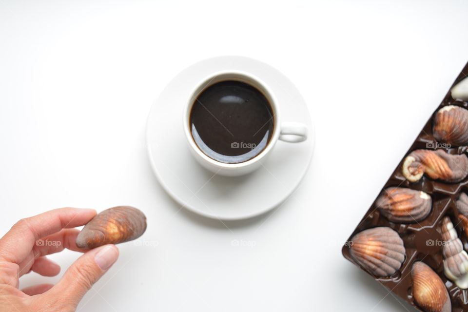 cup of coffee and chocolate candy in the hand on a white background top view, morning routine