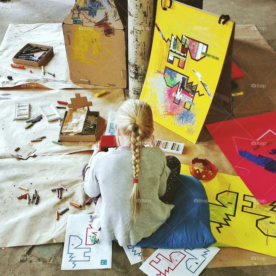 A girl sitting on the floor, playing on a tablet, surrounded by various toys