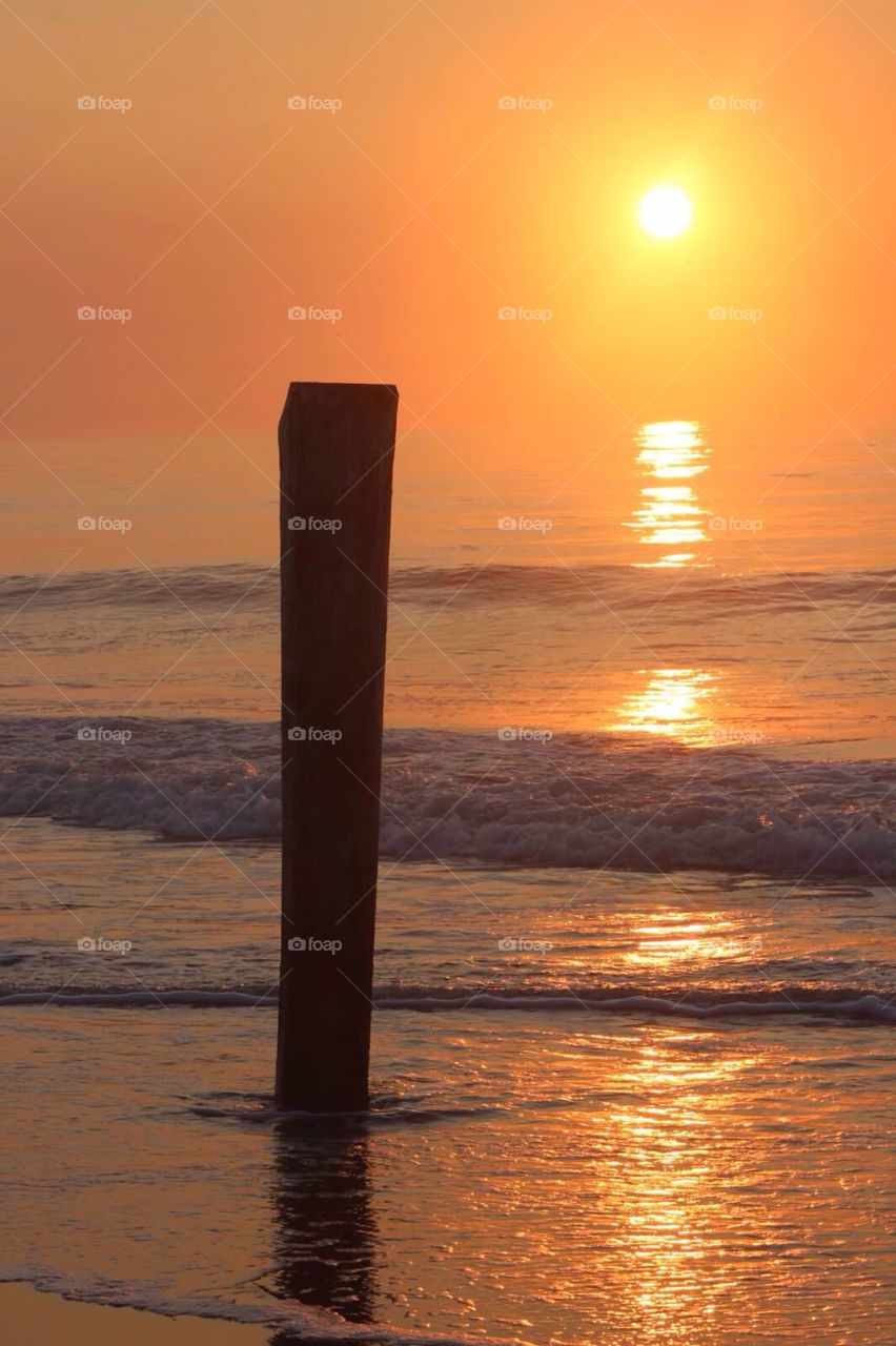 Post in the sand. . A lone post standing tall on the beach at sunrise. 