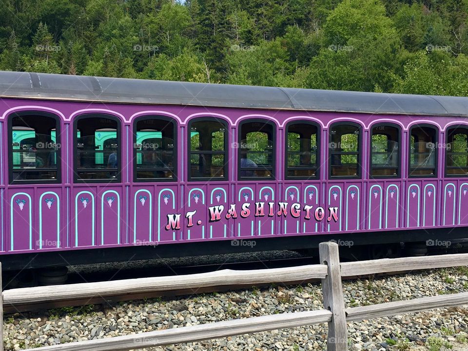 A striking purple passenger car rests at the Mount Washington Cog Railway station, its vibrant color standing out against the surrounding landscape.
