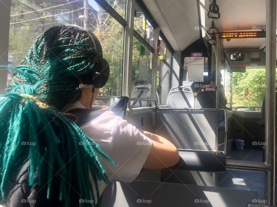 A girl with dreadlocks, headset and phone travels on a bus