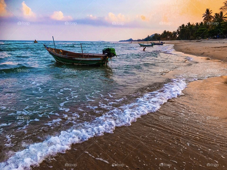 Romantic holiday vacation on tropical sandy beach seaside with fishing boats seen during sunset in southern Thailand - colorful ocean theme background