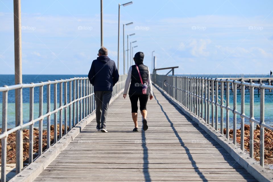 Couple walking away from
Camera toward ocean along long public Jetty 