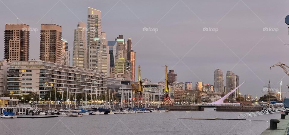 Buildings of the Puerto Madero neighborhood in Buenos Aires, river with some boats and in the middle the famous Puente de la Mujer. Sunset reflected in the windows of the buildings.