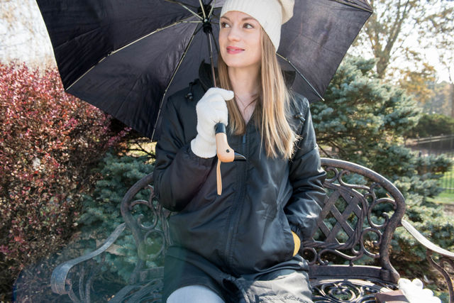 Young woman sitting on a bench outdoors while holding an umbrella