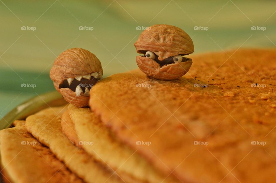 a small toothy nut resembling a crab or a sea shell bites its teeth into the cake. the second living nut with eyes has opened its shell and a small miniature on the kitchen table is looking at it.