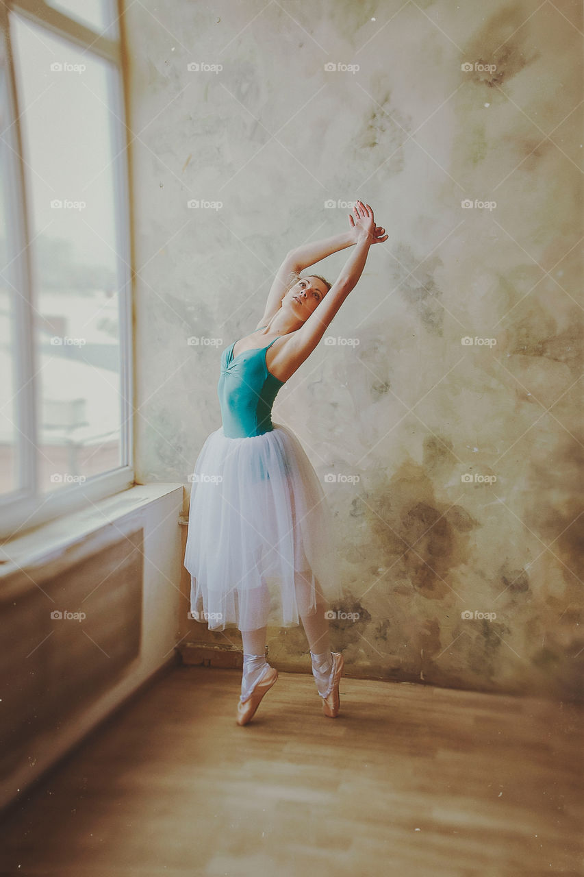 Young and graceful ballerina in pointe shoes and a tutu dances in a studio. Choreography and dancing classes concept. Creative ideas of ballet posing and performance.