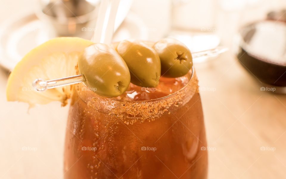 Beautiful cocktail simple and elegant Caesar on wood table with olives and lemon slice garnished with salt and pepper 