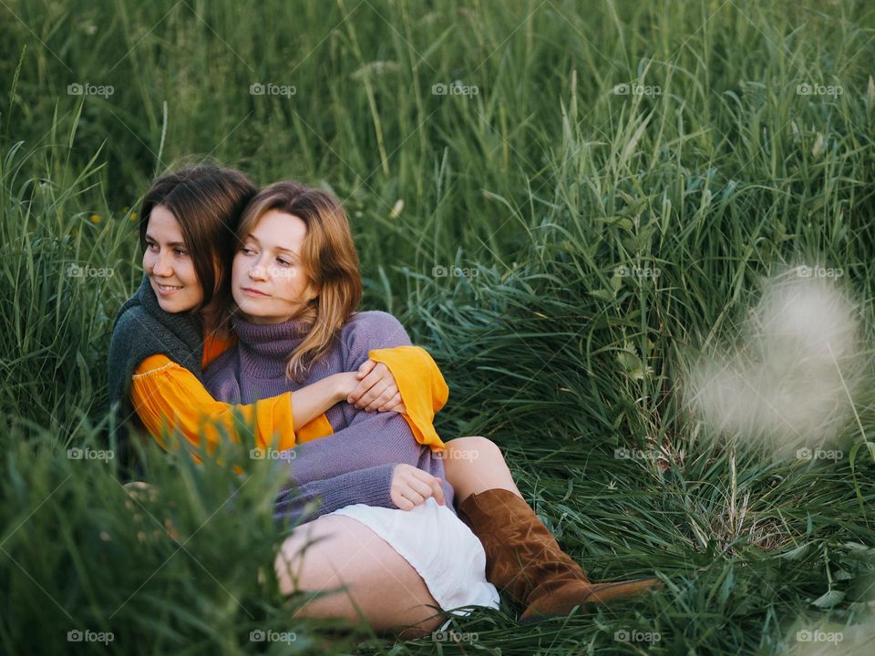 Two young beautiful woman’s sitting on a green grass in field in summer day, portrait of woman 