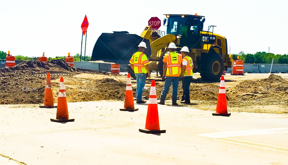 workers inspecting excavation at the road.  Machinery at use.