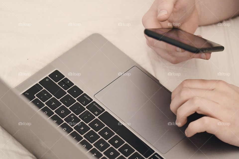 A man holding a phone and using his laptop computer