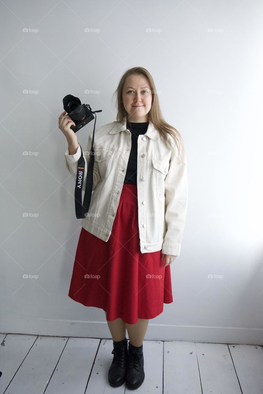 Lady in red skirt white jacket black t-shirt with camera smiling 