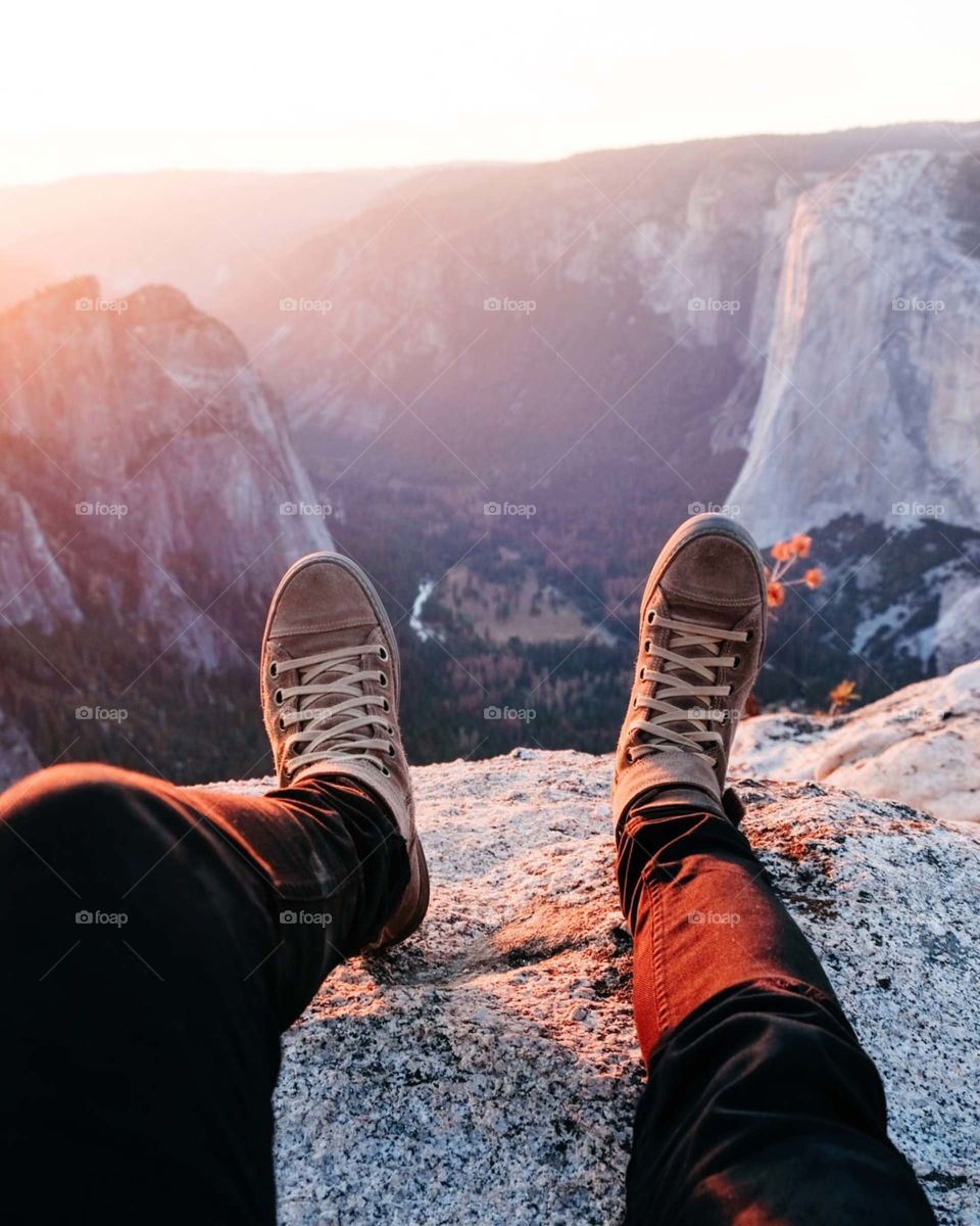 person wearing brown lace-up sneakers sitting on rocky mountain during daytime..