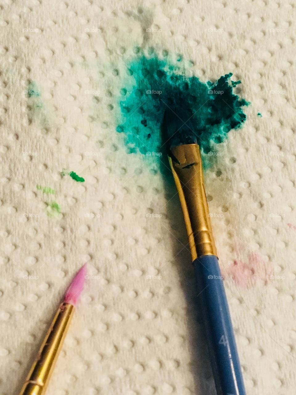 A close up of two used paint brushes on a paper towel. One of them is staining the paper towel a blue/green color 
