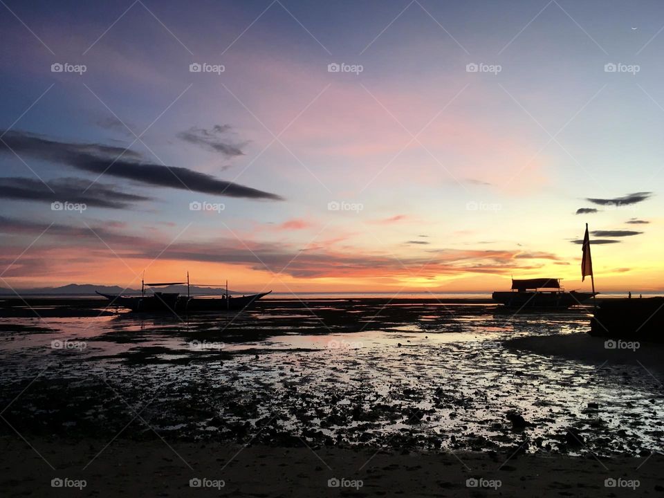 Silhouette of a boats on a low tide ocean against sun down at San Remigio Cebu Philippines. 