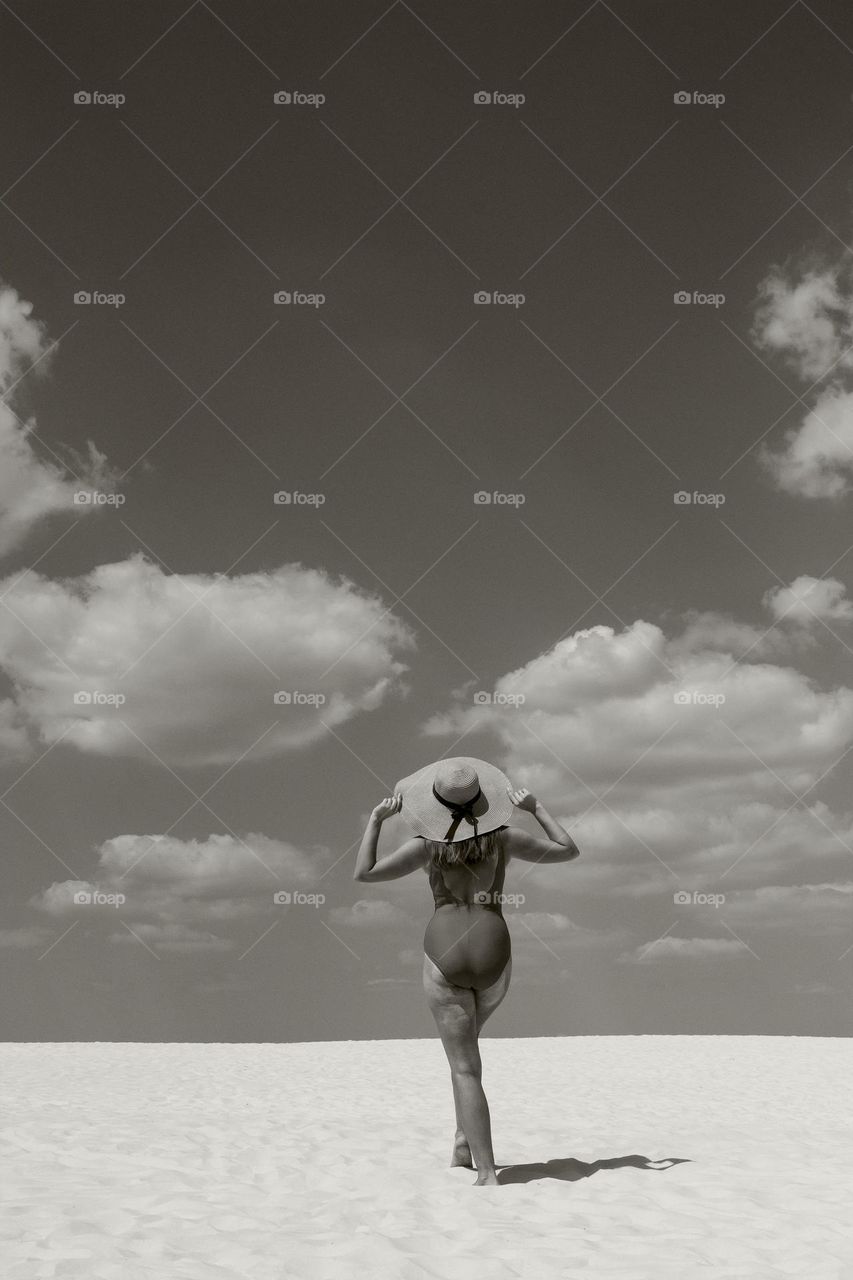 A girl in a bathing suit and a hat admires the clouds in the sky.