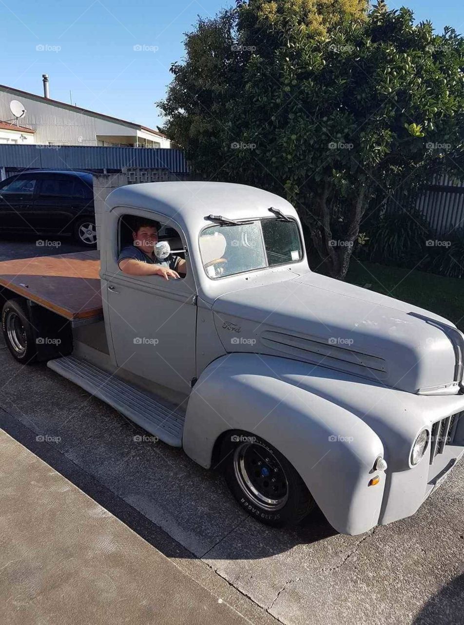 Young and Old unite. A young boy with no license. Sits in the drivers seat of this Ford jail bar pick up truck. Dreams are free. Imagination wild! One day when he is of age he will make it out of the driveway.