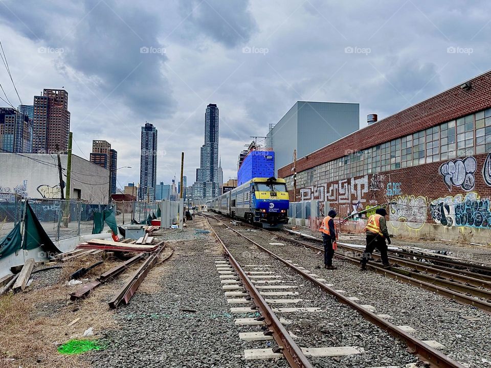 The „Long Island Railroad“ train is disappearing into the distance far away here at „Borden Avenue“ and „11th Street“ by the „Pulaski Bridge“ in LIC, Queens and the maintenance workers have started working again. 2023. Hypnotic Productions
