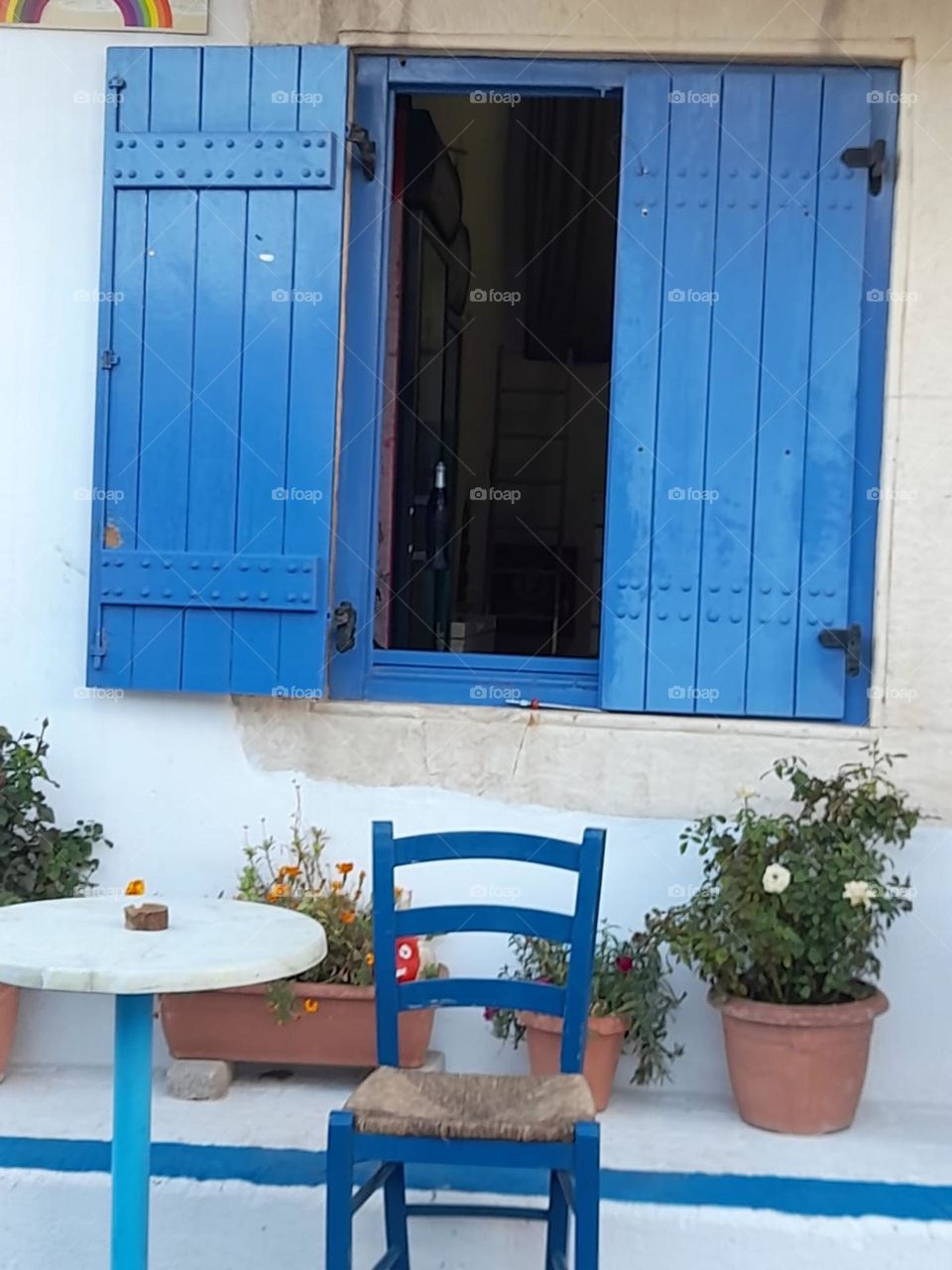 greek blue window shutters on white wall. tabke and chair