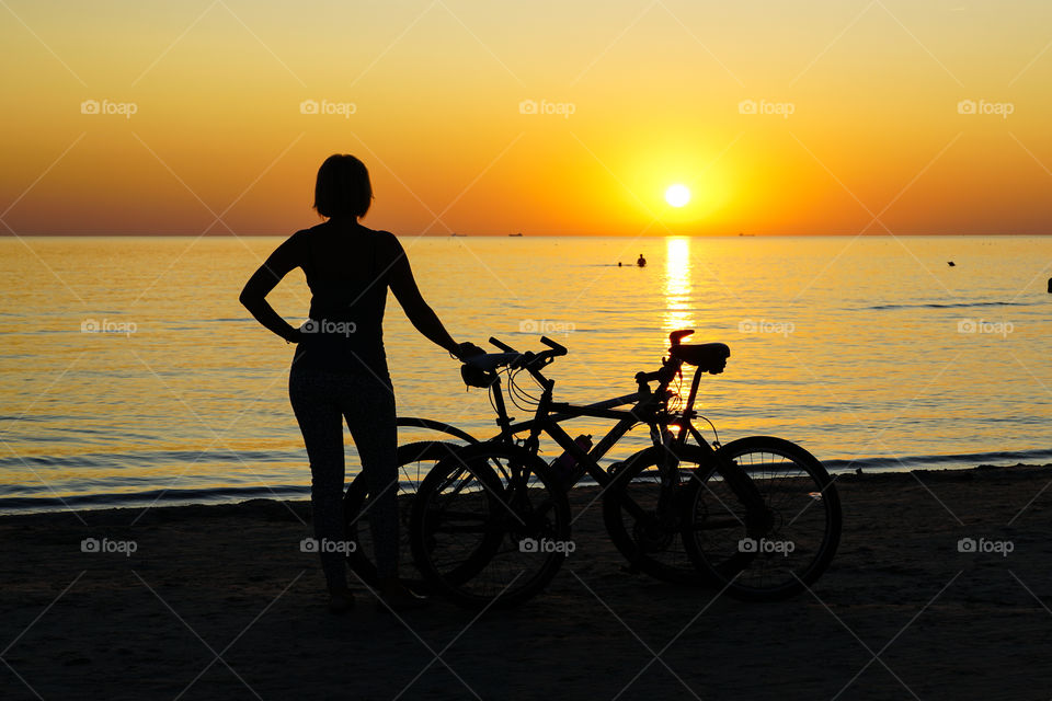 sunset by the sea, women and bicycle silhouettes on the sea background