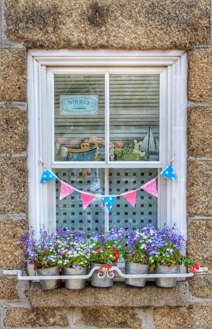 A Cornish Country Window. A small cottage window with bunting and flowerpots arranged below.