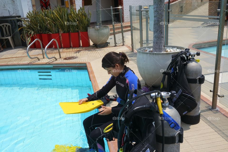 Chica con equipo de buceo en el borde de una piscina.