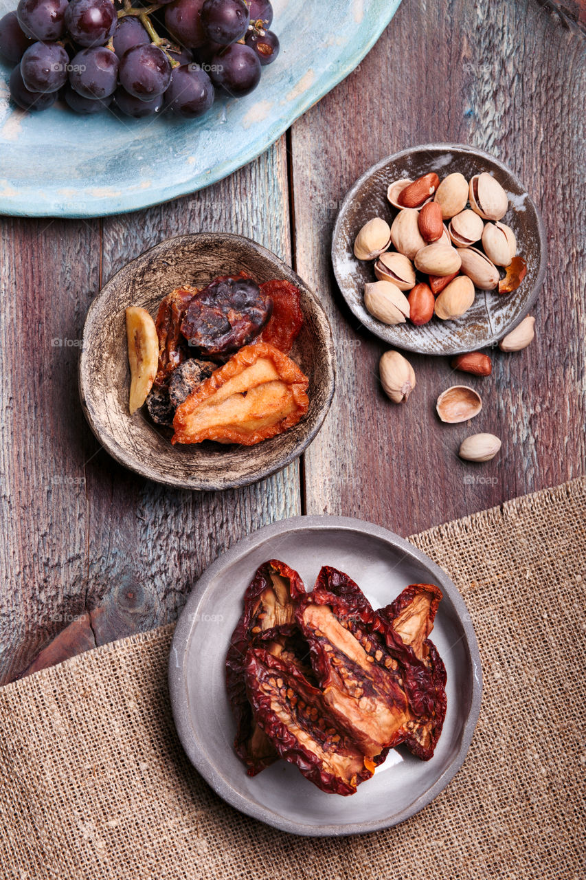 Dried fruits and nuts in handmade pottery bowls on old wooden table from above