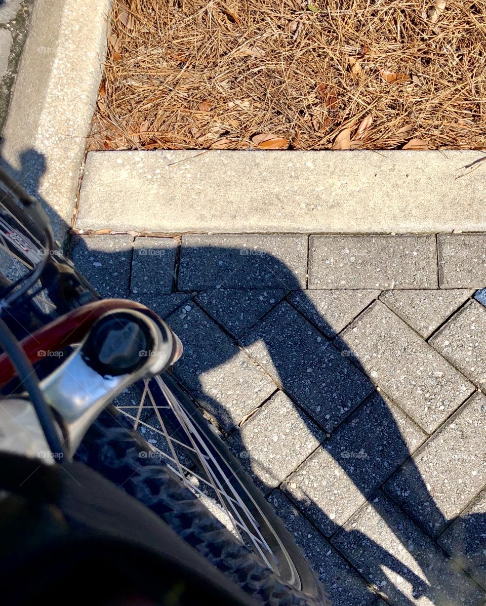 Shadow of bicyclist leg and part of front wheel without bicyclist in frame