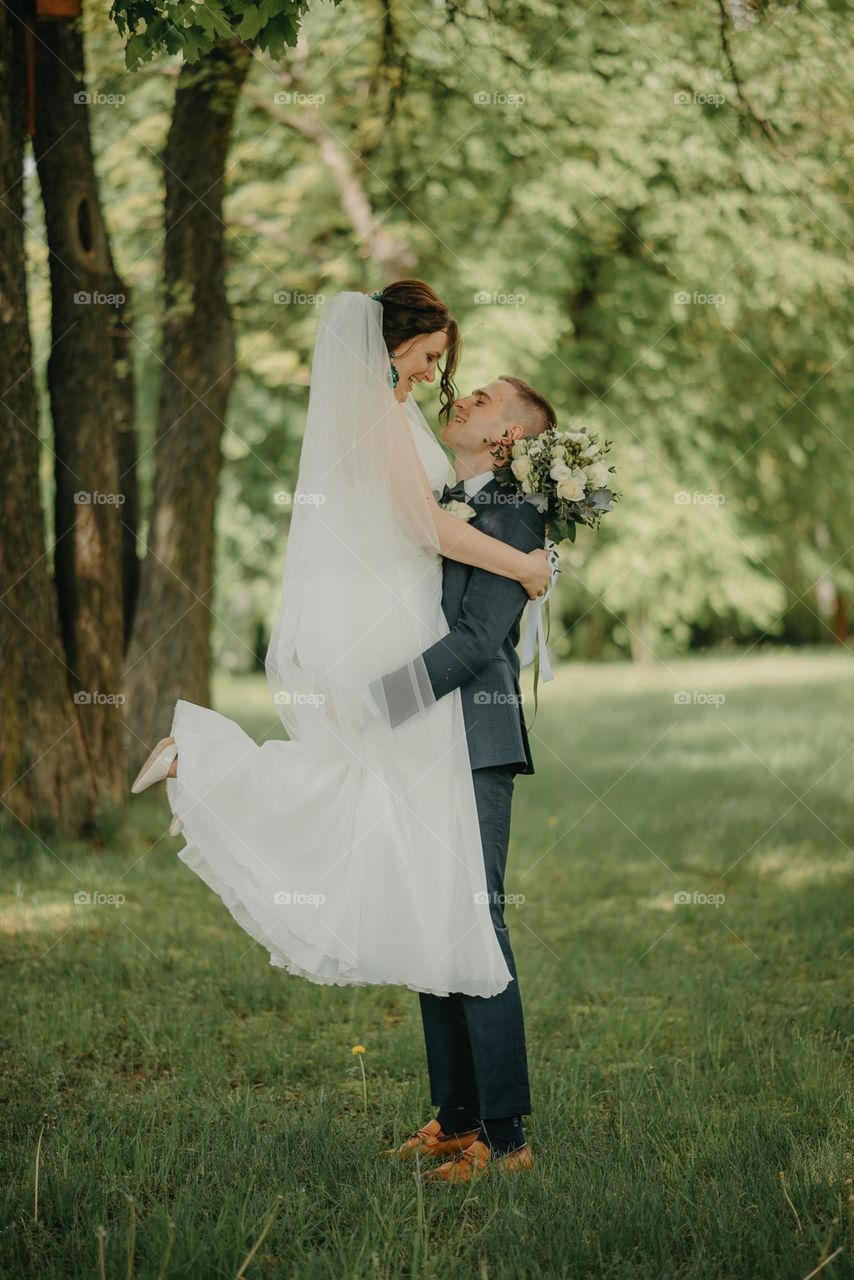 A groom holds his bride in his arms before a sweet kiss in a city park