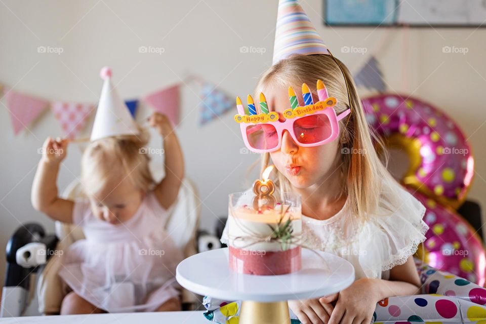 Little Caucasian girl celebrating eighth years old birthday at home and blowing candle on cake 