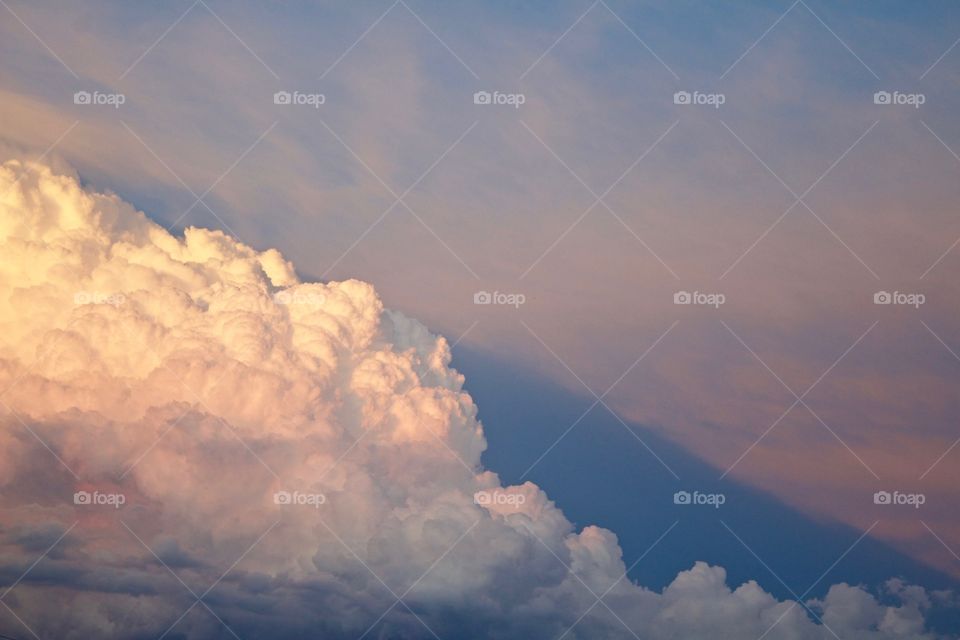 A large cumulonimbus cloud creates an angled shadow and rays from angled sunlight against a hazy blue sky 