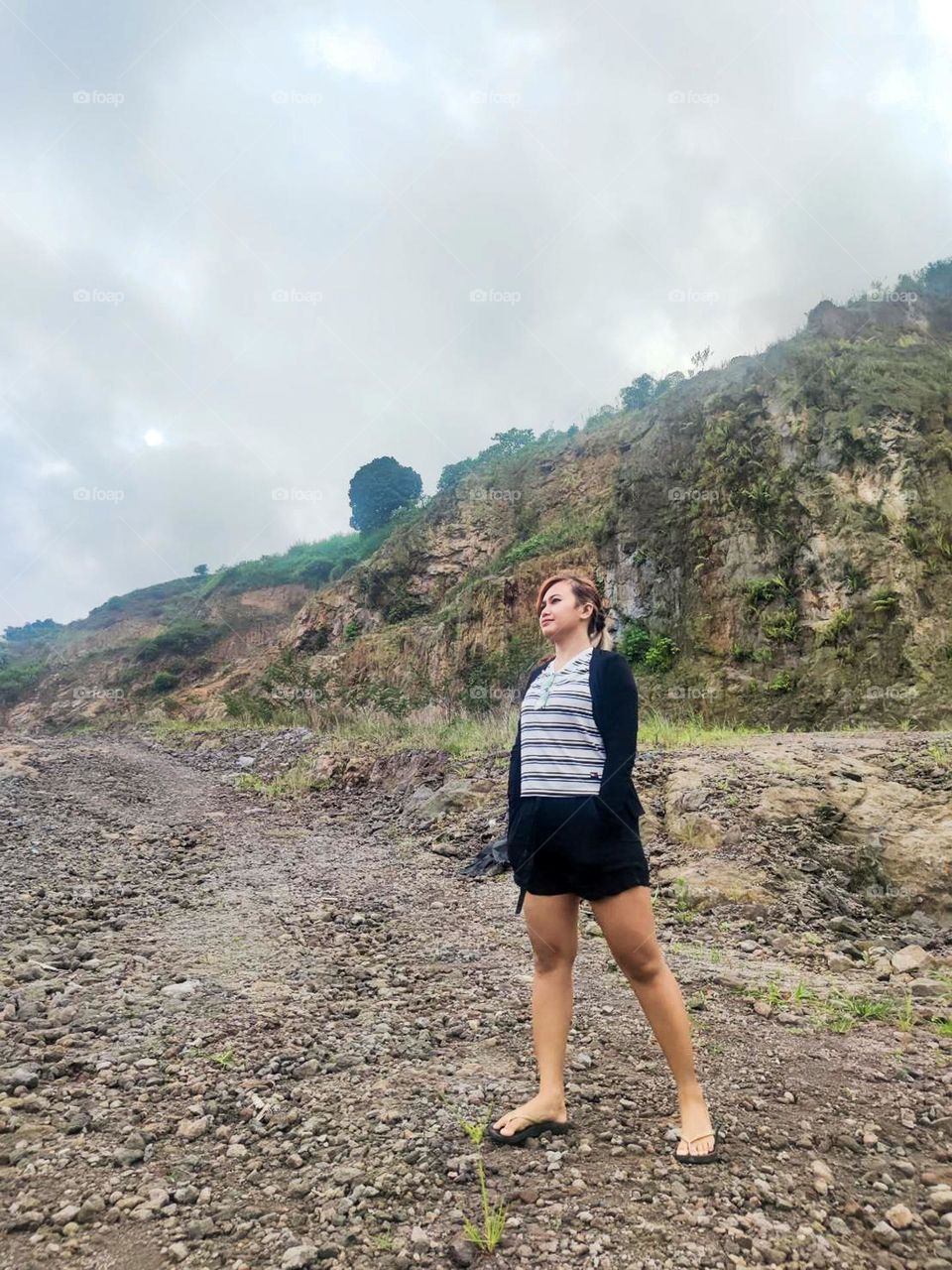 Young woman standing on a rocky area with a hill or cliff in the background