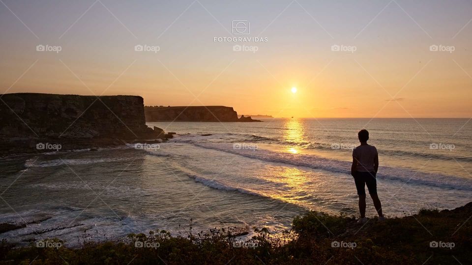 A woman contemplates the sun set in front of the ocean
