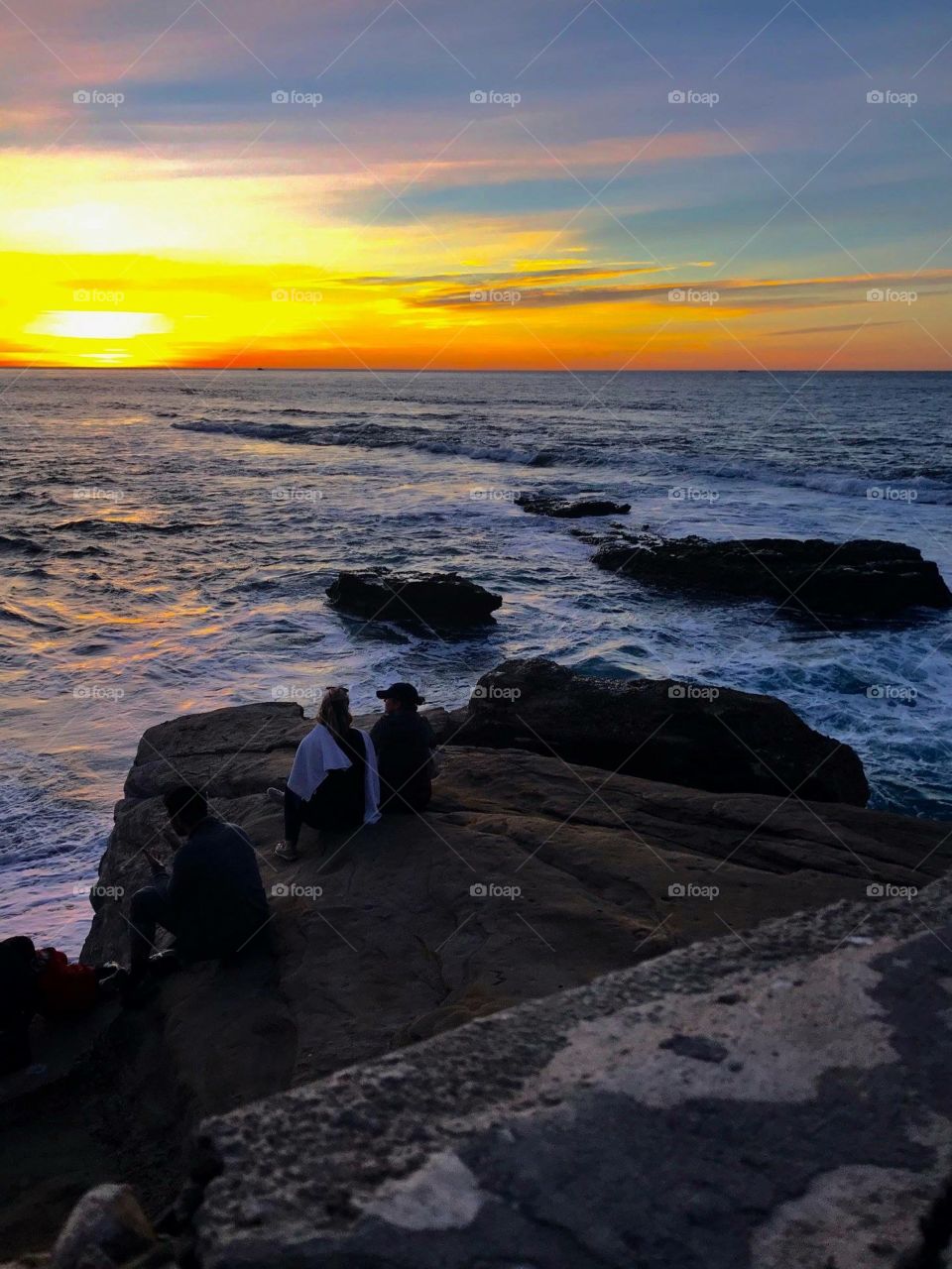 Two people watching the sunset over the Pacific on a rock 