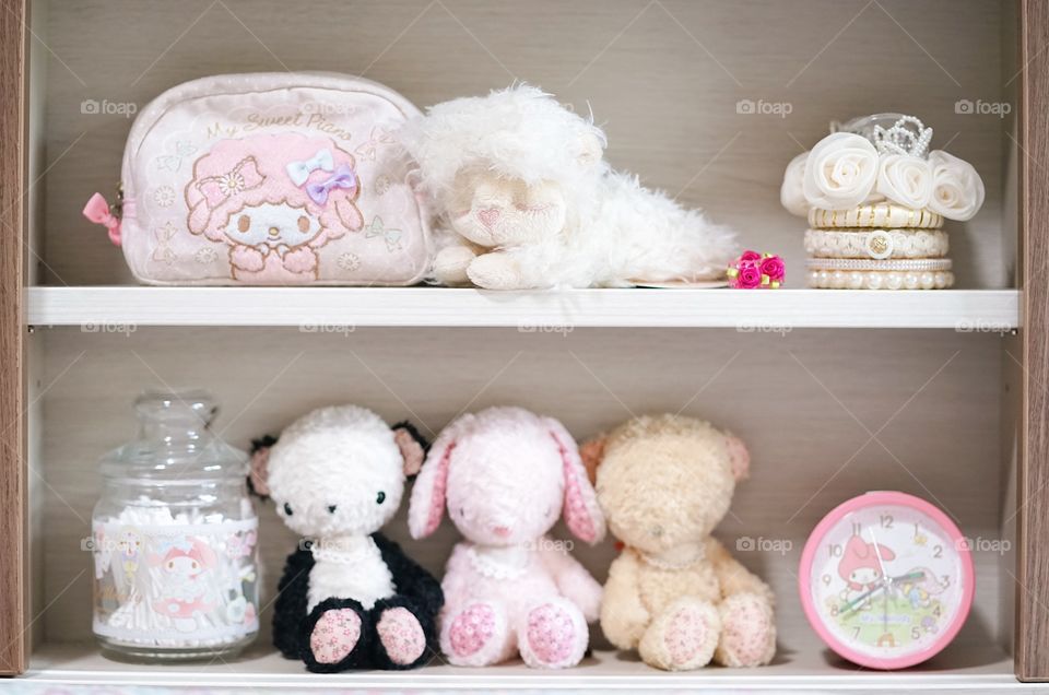 Cute soft plushes. Lovely dolls are sitting on the little girl's headboard and other cute accessories. Selective focus on kawaii sheep plush doll on top shelf.