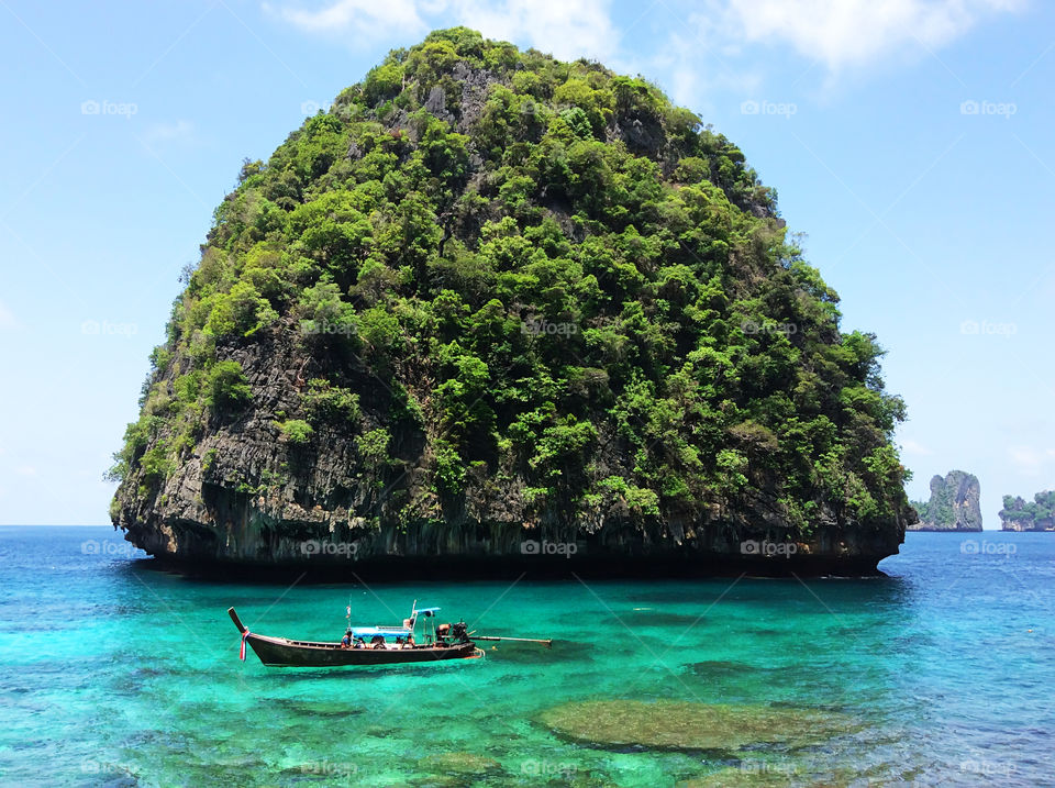 Boat with tourists swimming in turquoise clear sea water nearby green tropical island in Thailand