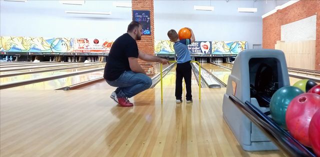 dad helps the kid play bowling