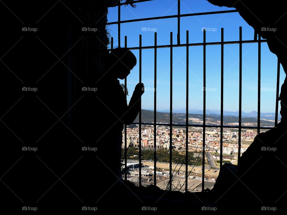 Silhouette of young woman standing by metallic bars with view on Gibraltar.