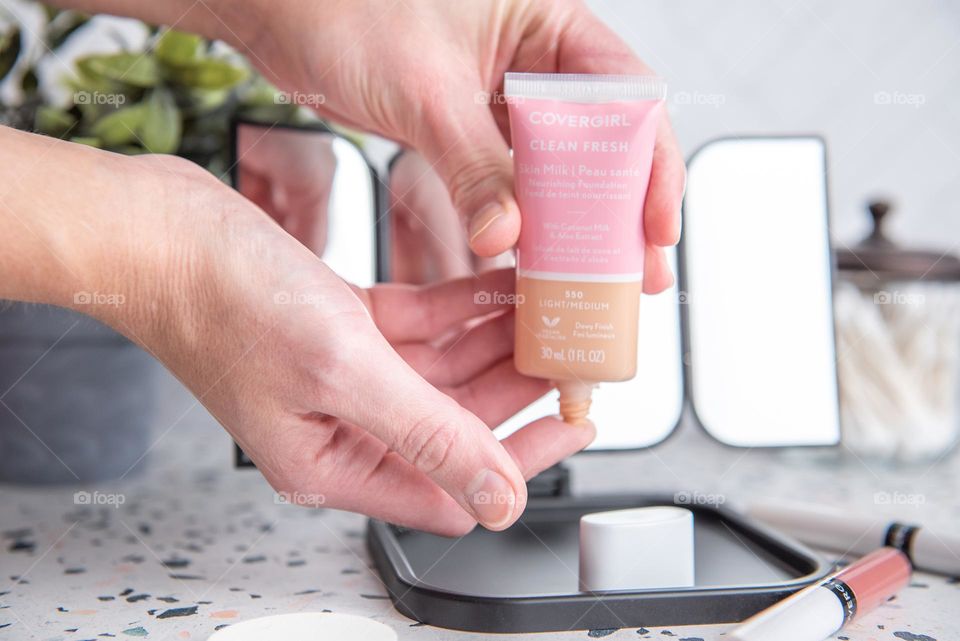 Closeup of a woman dispensing liquid foundation onto her fingertips in front of a cosmetics mirror 