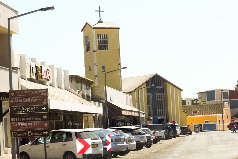 Town view of vehicles parked on the road, road signs and a tall church building in the urban center. 