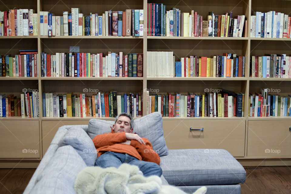 Man sleeping on a couch in front of a bookshelf 